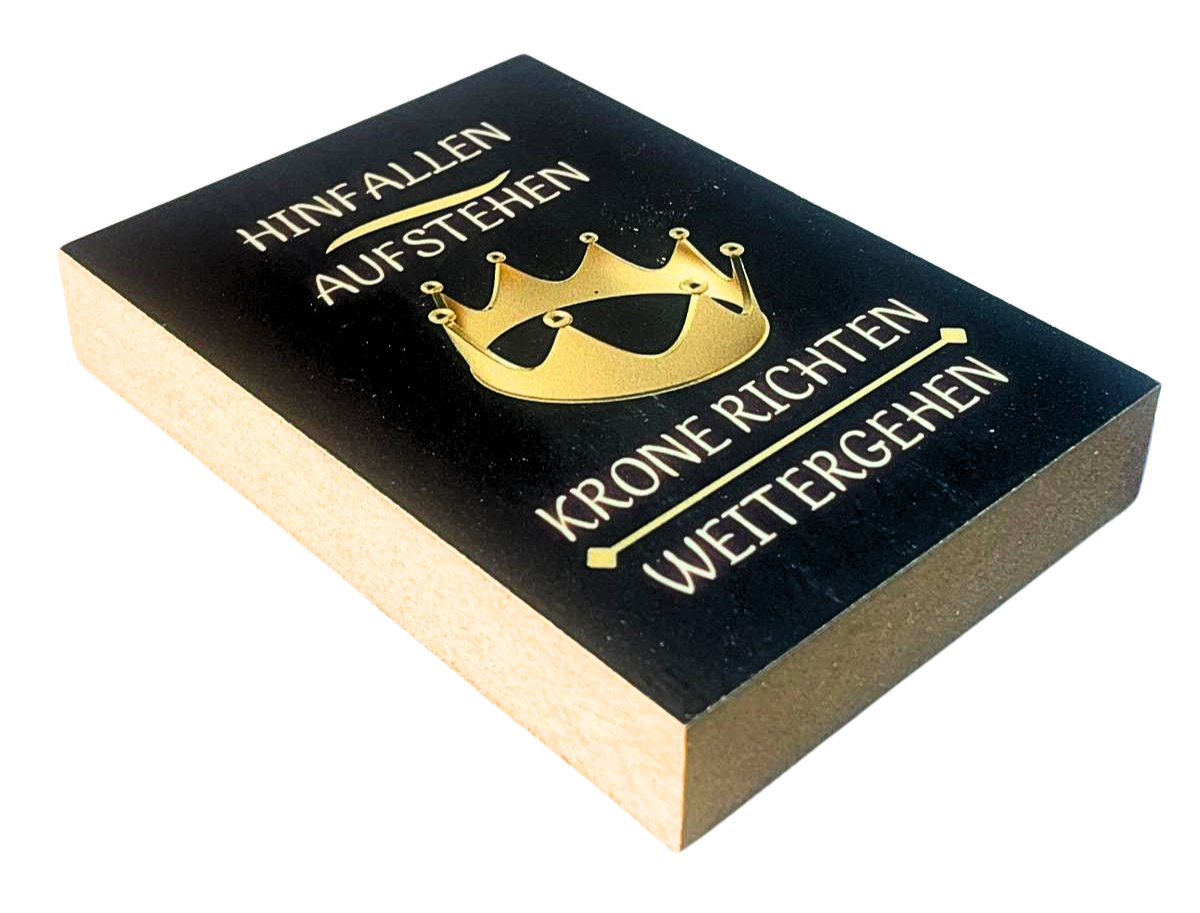 Liegende Ansicht Holzbild mit schwarzem Hintergrund und goldener Krone, mit dem Spruch "Hinfallen, Aufstehn, Krone richten, weitergehen"