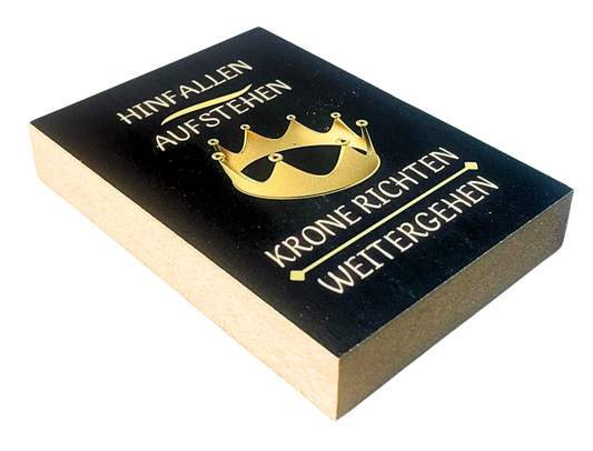 Liegende Ansicht Holzbild mit schwarzem Hintergrund und goldener Krone, mit dem Spruch "Hinfallen, Aufstehn, Krone richten, weitergehen"