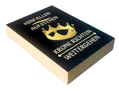 Liegende Ansicht Holzbild mit schwarzem Hintergrund und goldener Krone, mit dem Spruch "Hinfallen, Aufstehn, Krone richten, weitergehen"