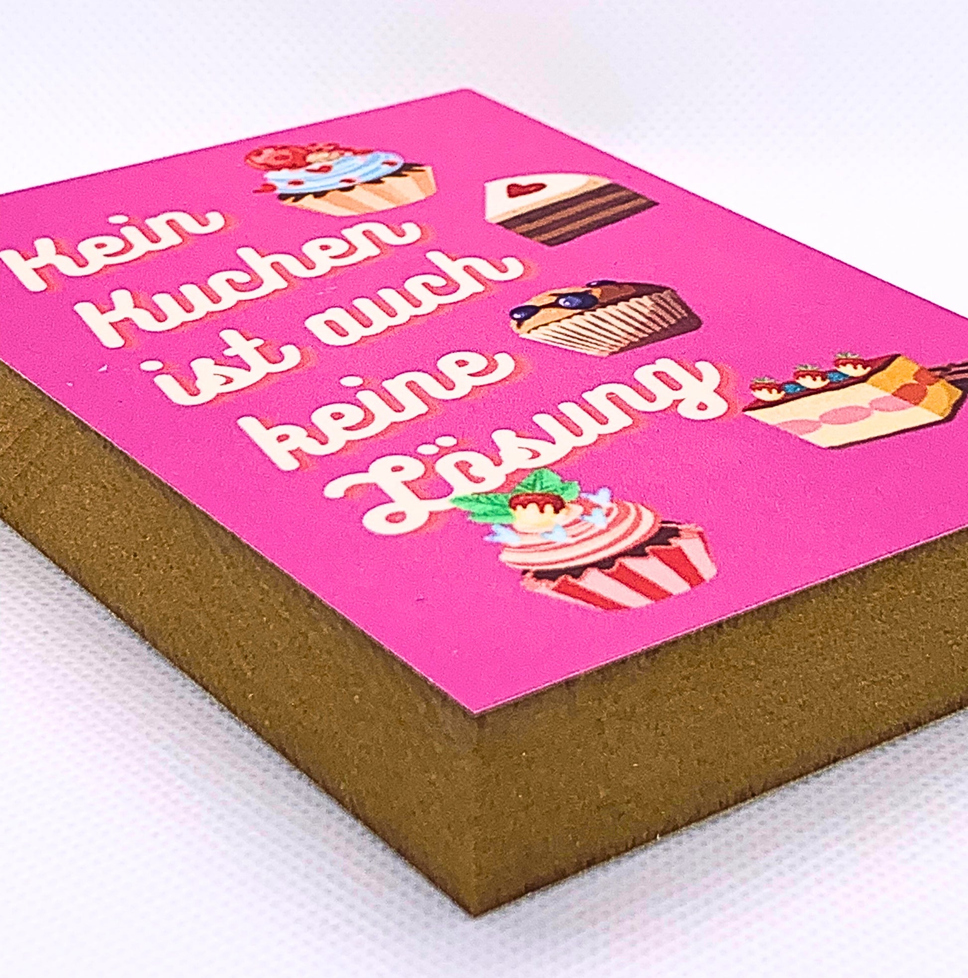 Liegende Ansicht Holzbild  mit pinkfarbenem Hintergrund auf dem Zeichnungen mehrerer Kuchenstücke zu sehen sind siwei der Spruch Kein Kuchen ist auch keine Lösung.