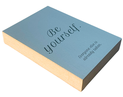 Liegende Ansicht Holzbild mit schwarzer Schrift auf blaugrauem Hintergrund "Be yourself. Everyone else is already taken."