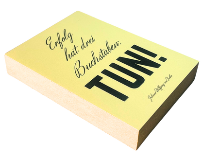 Liegende Ansicht Holzbild mit gelbem Hintergrund und schwarzem Text "Erfolg hat drei Buchstaben: Tun!"