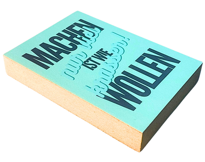 Liegende Ansicht Holzbild mit Schrift auf türkisem Untergrund "Machen ist wie Wollen, nur viel krasser!"